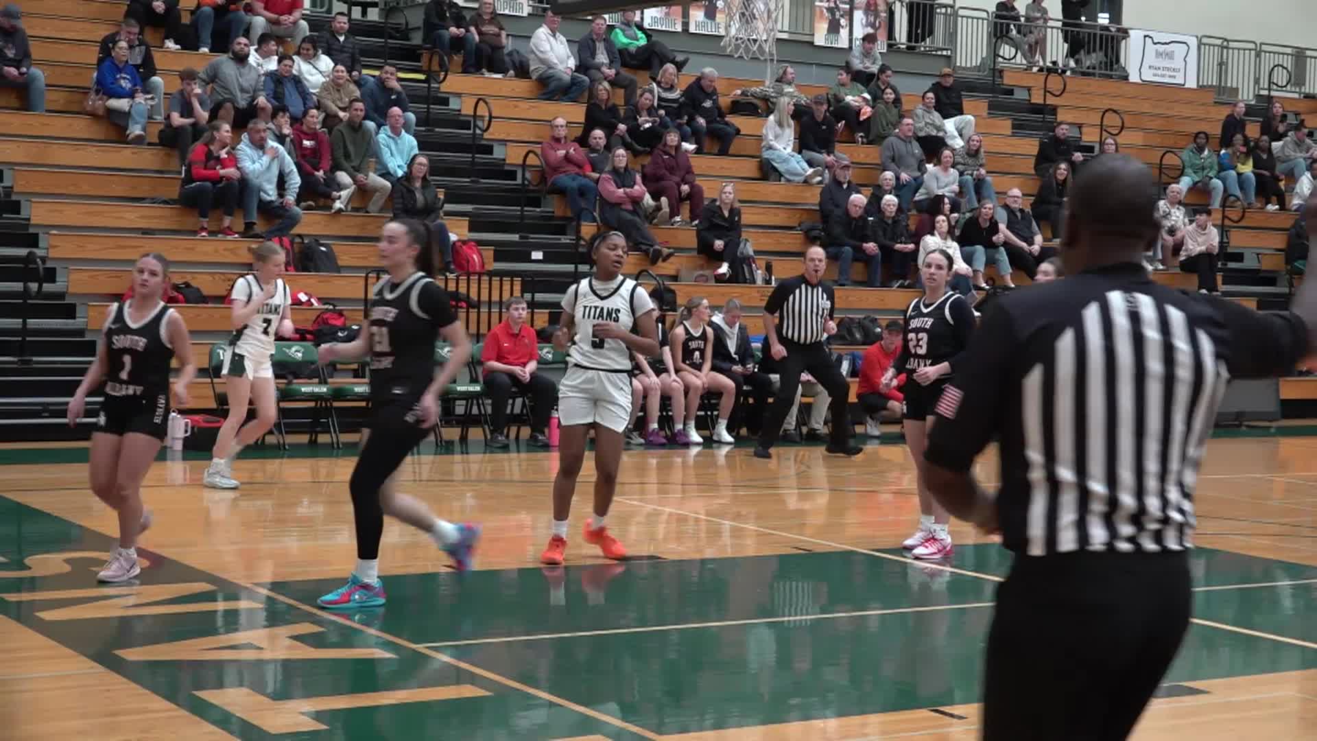 basketball court with two girls teams at the basket, spectators in the stands in the background