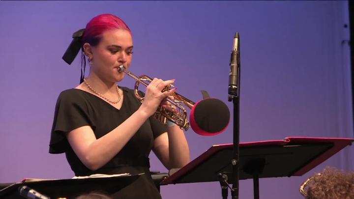 Girl dressed in black playing a trumpet. Purple background