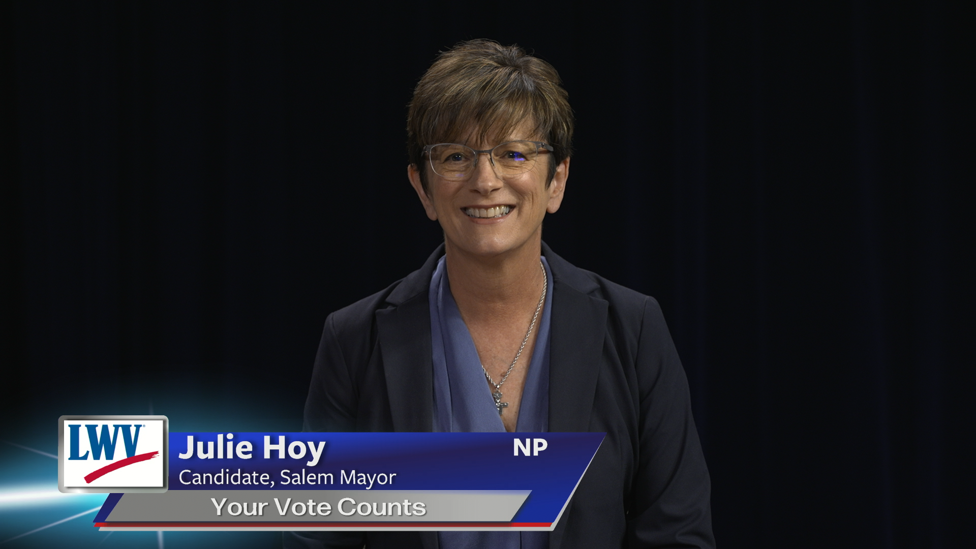 Black background. Woman in the middle with short hair and glasses, wearing blue. League of Women Voters logo in red, white and blue to the bottom left. White words on a blue background low middle: "Julie Hoy Candidate, Salem Mayor Your Vote Counts NP" 