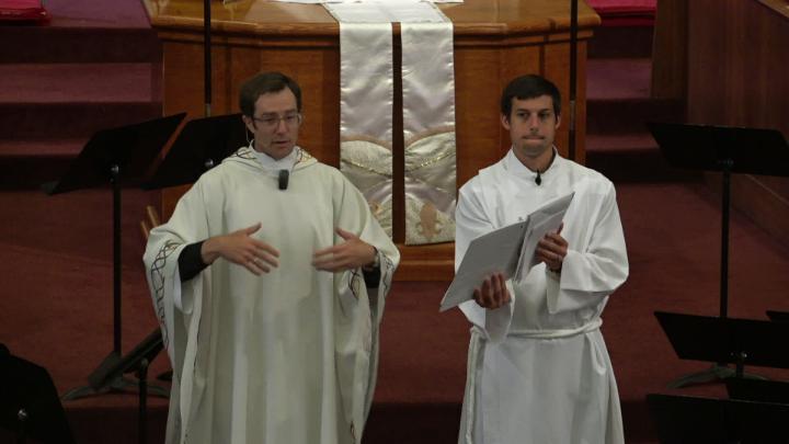 Priest standing in front of an alter and banner with a cross on it.