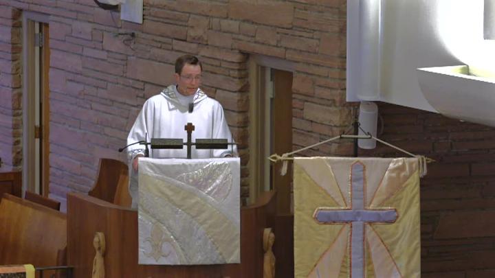 Priest standing behind an alter and banner with a cross on it.
