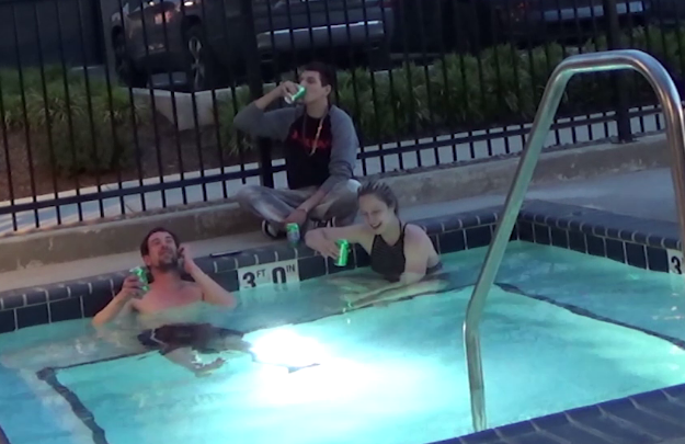 Man and woman in a pool. Another man sitting on the deck behind woman, drinking something from a can.