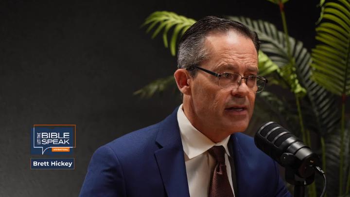 Man in a suit and glasses seated behind a podcast mic. Dark walls and a plant in the background. Blue Let the Bible Speak logo in the lower left corner.