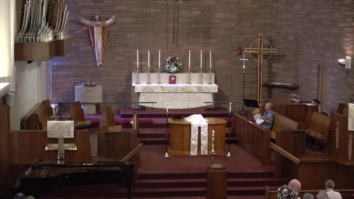 wide shot of the front of a church with brick walls, a statue of Jesus back left, a;ter baack center, pews to the right