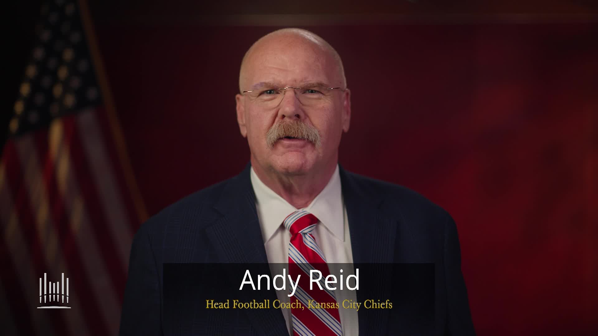 Maroon background with an American flag to the left. Andy Reid in a suit in the middle