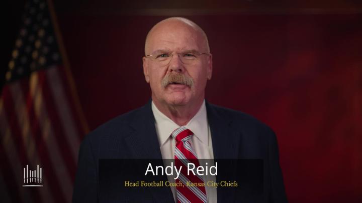 Maroon background with an American flag to the left. Andy Reid in a suit in the middle