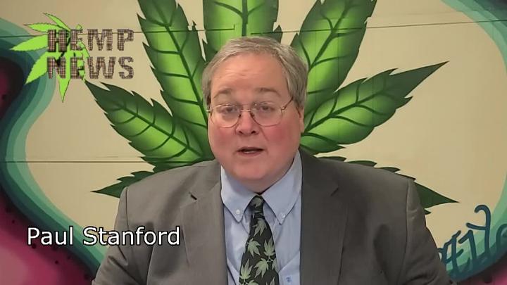 Man in glasses and a suit seated in front of a large green cannabis leaf. the words "Hemp News" upper left corner