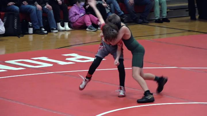 Kids dressed in wrestling singlets on a red mat