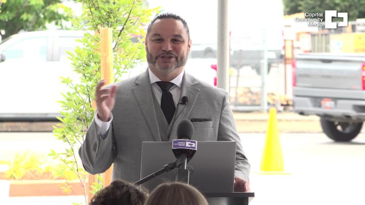 Man in a grey suit standing outside in front of a mic