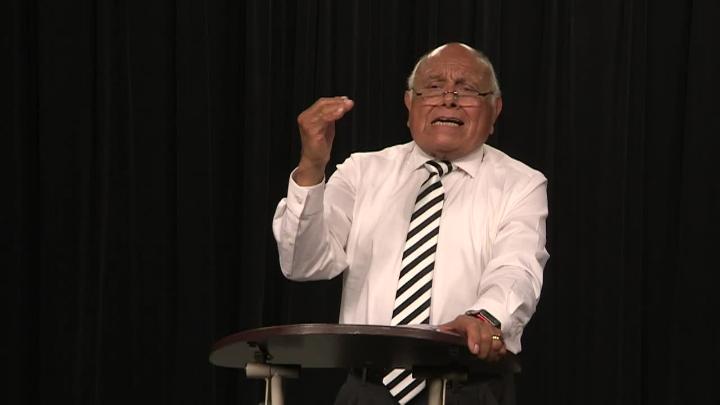 Black curtain background. Older man in a white shirt behind a podium