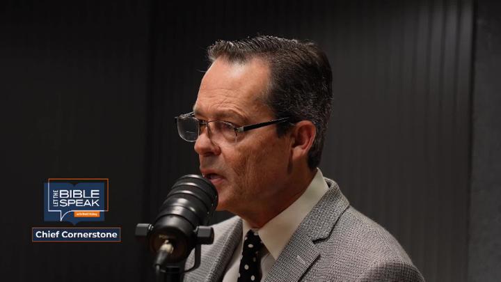 man in a suit in front of a podcast mic. dark walls behind him. Let the Bible Speak logo in blue in lower left hand corner