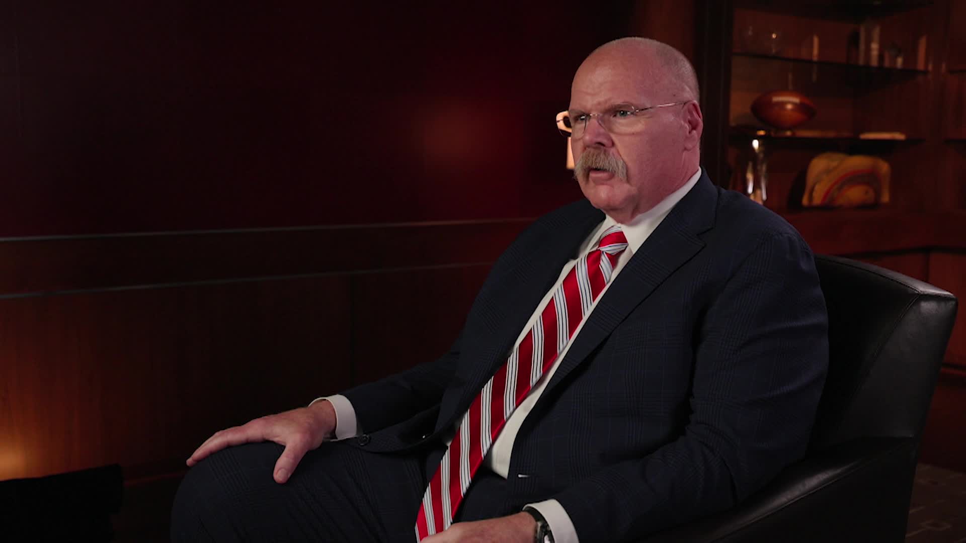 Andy Reid seated to the right wearing a dark suit