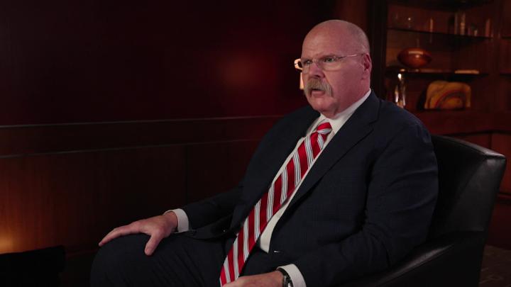 Andy Reid seated to the right wearing a dark suit