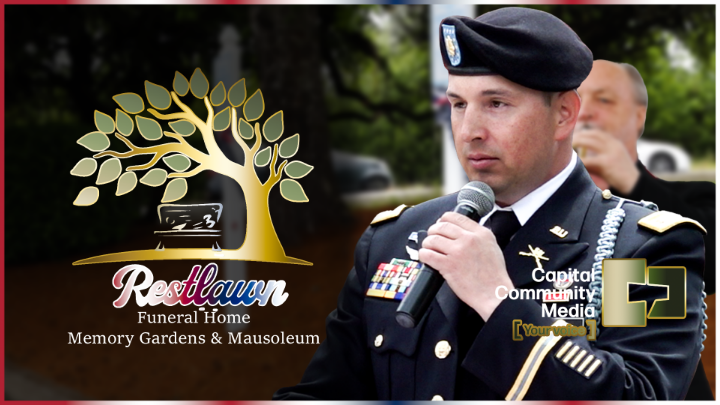 Picture of a military person holding a mic on the right and a weeping tree with Restlawn under it on the left side.