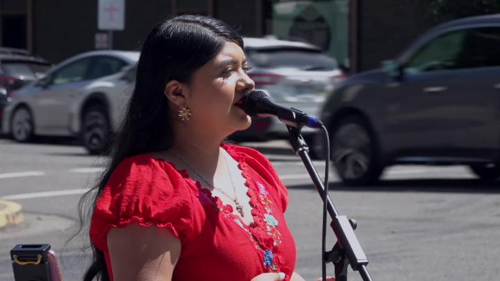Woman in a red dress singing in front of a mic as cars pass by.