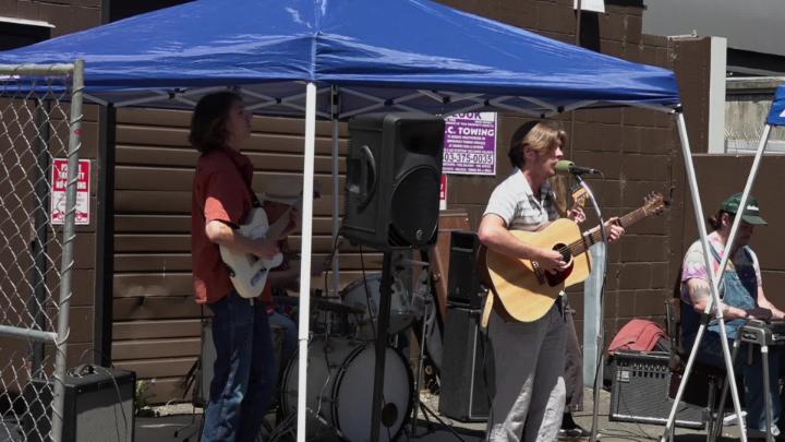 Musicians playing guitar under a blue awning 