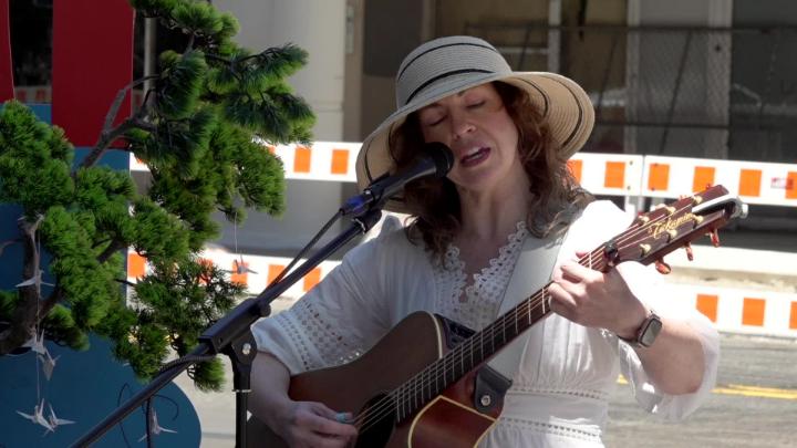 Woman dressed in white singing into a mic and playing guitar