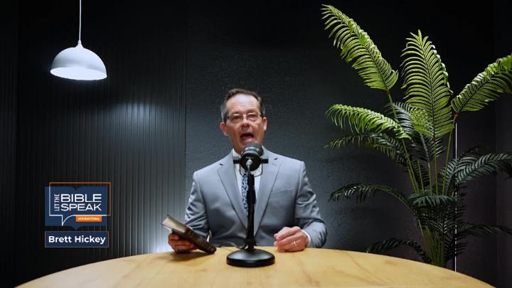 Man wearing a suit seated at a table behind a podcast mic. Plant to the right. "Let The Bible Speak" logo bottom left