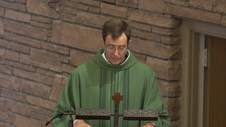 Priest in green with a brick background
