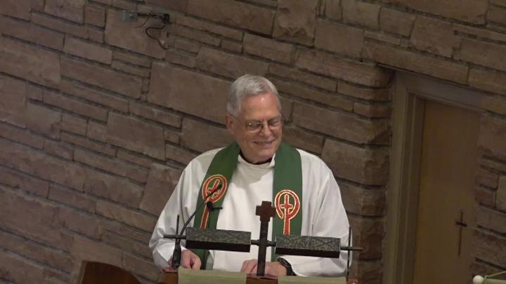 Priest in white standing in front of a brick wall