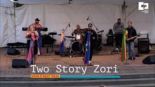 White tent background with various musicians on stage. "Two Story Zori" at the bottom