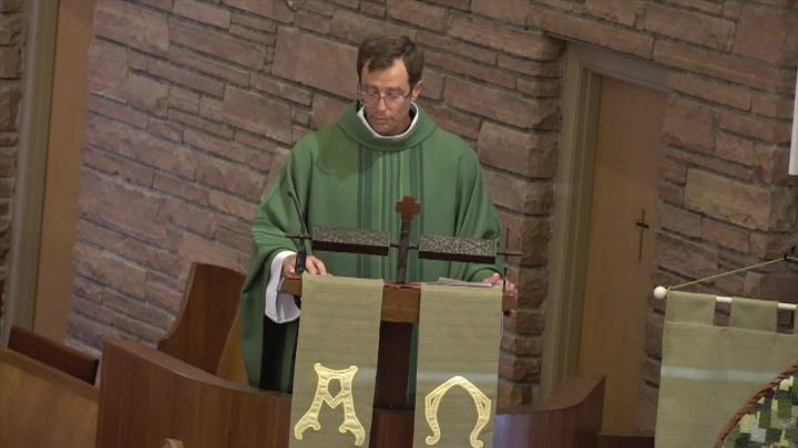 Priest in a green robe standing behind a podium in front of a brick wall