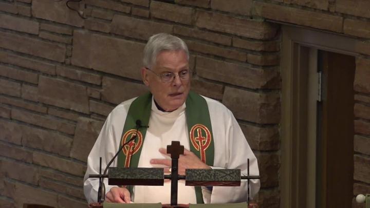 Priest in a white robe in front of a brick wall