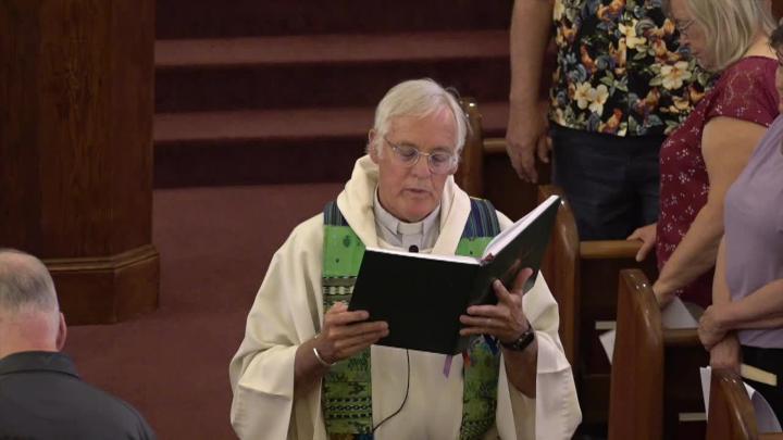 Priest in a white robe and green scarf reading from a bible