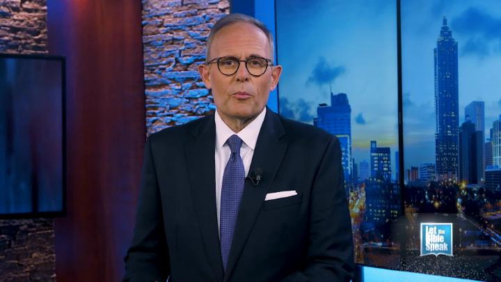 Man in a suit and glasses standing in the middle. A cityscape in the background