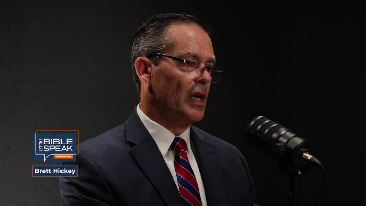 Man in a suit and glasses looking right, talking into a podcast mic. Blue and orange Let the Bible Speak logo bottom left