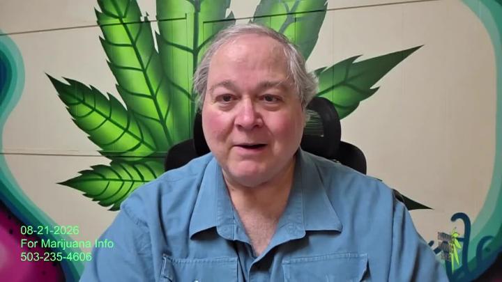 Man in a blue button up shirt with a white brick wall and green cannabis leaf in the back