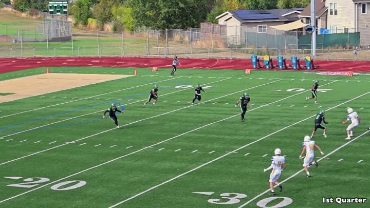 Outside football field with players dressed in black uniforms in the center and white uniforms to the right.