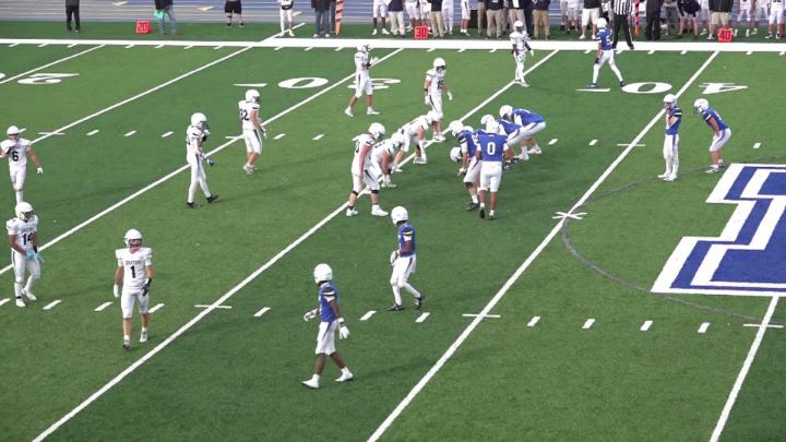 football field with players dressed in all white uniforms and players in white and blue uniforms are lined up.