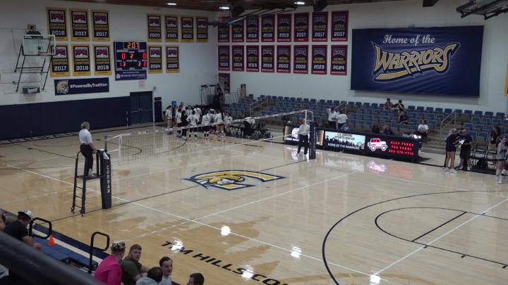 Volleyball court with refs at the net. Banners in the background.