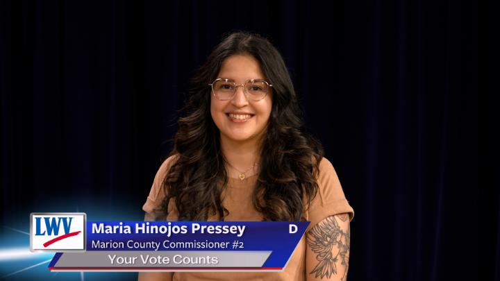 Black background. Woman in a tan t-shirt and glasses in the middle. Lower thirds to the bottom left with red, white and blue LWV logo. White words on a blue background: Maria Hinojos Pressey Marion County Commissioner #2 Your Vote Counts D