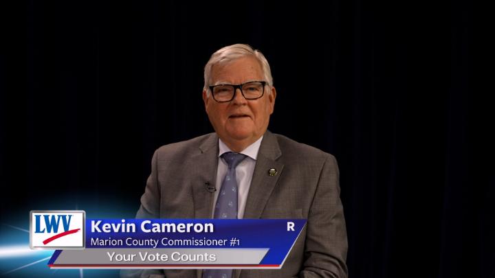Black background. Man in a grey suit and purple button up in the middle. Lower thirds to the bottom left with red, white and blue LWV logo. White words on a blue background: Kevin Cameron Marion County Commissioner #1 Your Vote Counts R