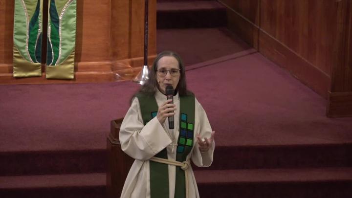 Woman priest in a white robe and green stole standing in the middle.