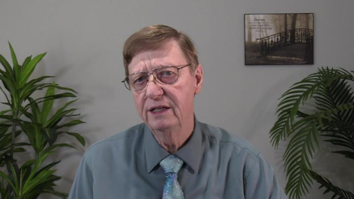 Man in a blue button up and tie seated in the middle. Plants in th background.