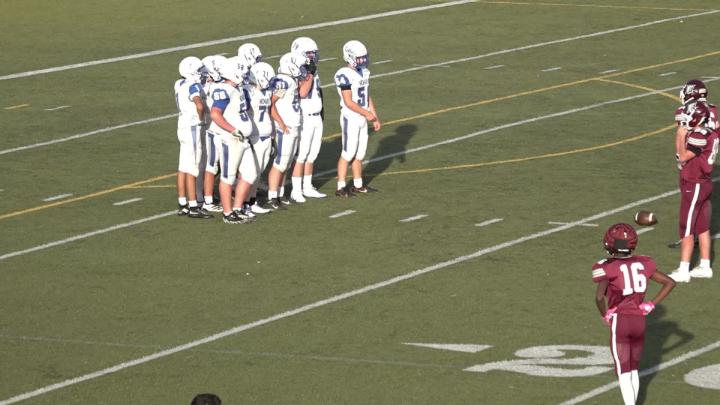 Football field with players dressed in white uniforms on it.