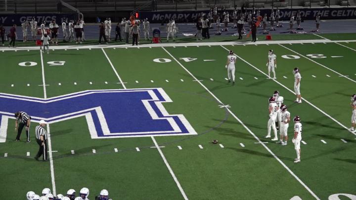 green football field with a large painted blue and white "M" to the middle left. Players in white uniforms scattered on the field.