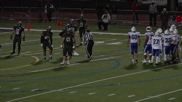 football field with players in black uniforms and other players in white and blue uniforms
