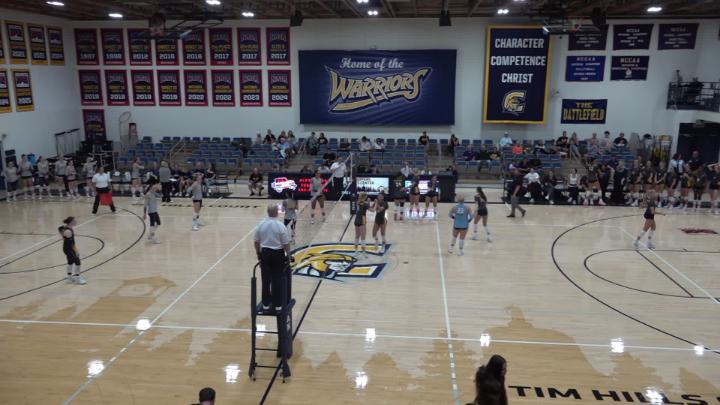 Basketball court with a a volleyball net across and players on the court