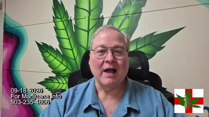 Man seated in the middle wearing glasses and a blue button up. White brick wall and green cannabis leaf in the background.