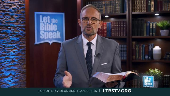 Man in a grey suit standing in the middle holding a bible. Bookshelf in the background on the right. Blue and white Let the Bible Speak logo back left.