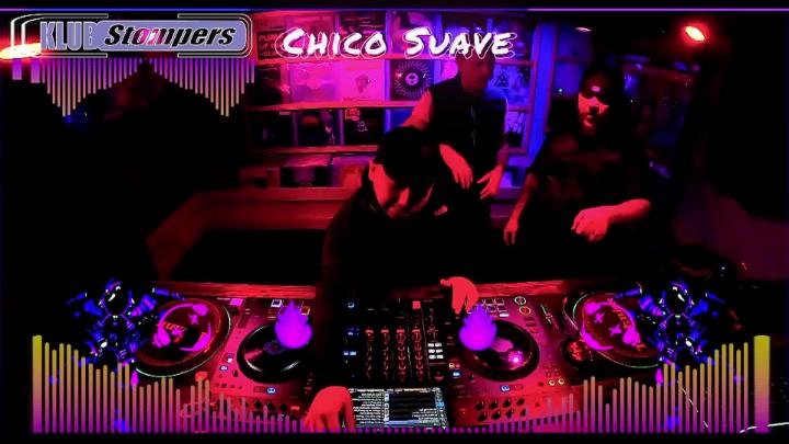Red and purple lights make picture red and purple toned. Man in a hat standing behind turntables. White words top middle:"Chico Suave"