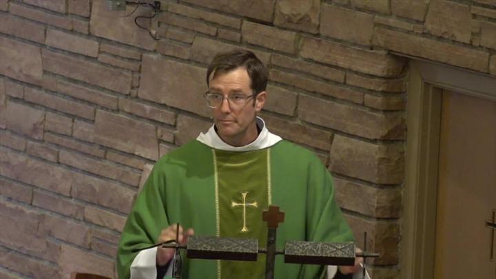 Priest in a green robe with a brick background