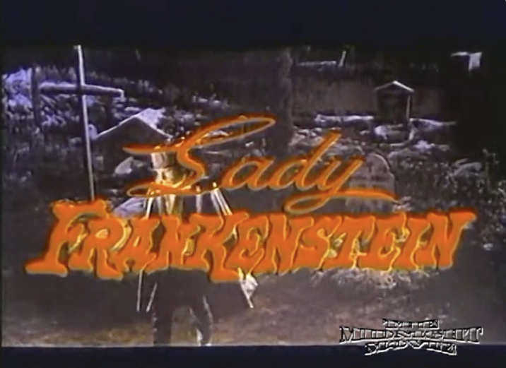 Dark graveyard in background with a cross to the left and large tombstone to the right. Man in top hat and cape walking to the left. Red wording in forefront saying Lady Frankenstein and The Midnight Movie in lower right corner.