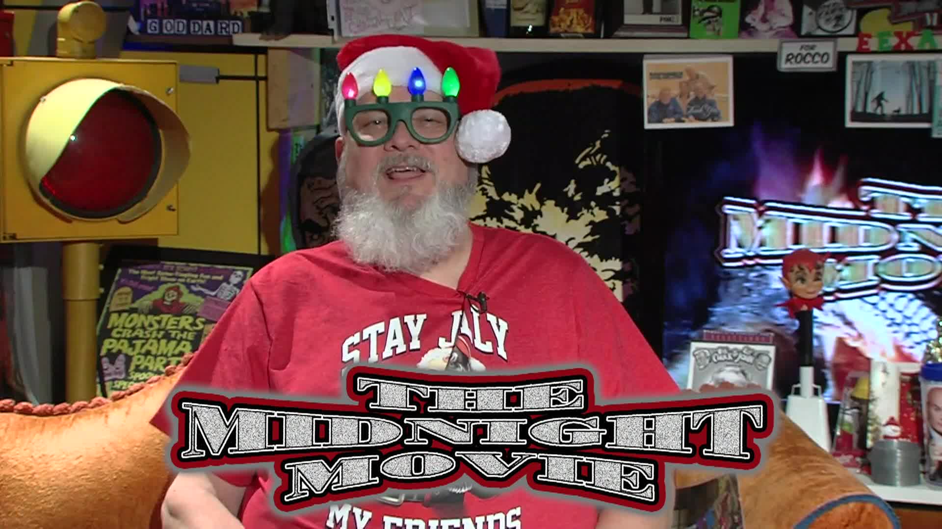 Man in red and wearing a santa hat with a busy background. White, red, and black "The Midnight Movie" logo on the bottom middle
